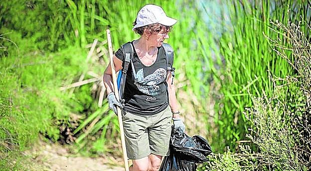 Una mujer recoge basura en un espacio natural.