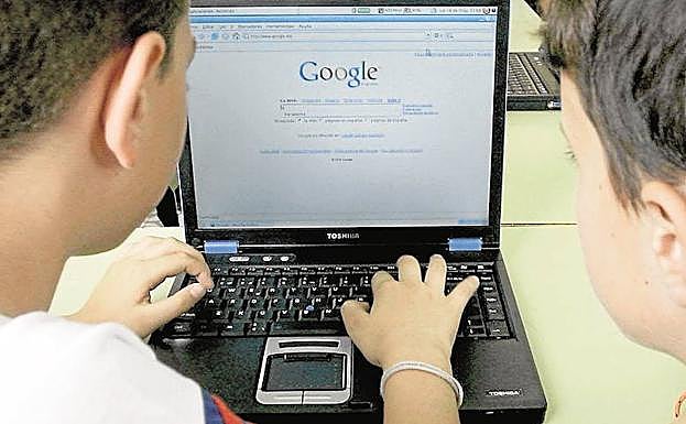 Dos niños aprender a usar el ordenador en el colegio. 