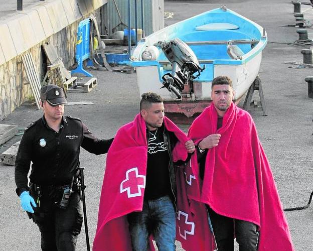 Un policía, en el puerto con dos inmigrantes llegados en patera.