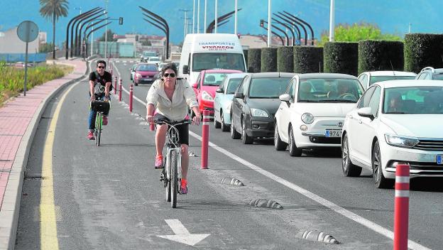 Ciclistas circulando por el carril bici en dirección a Puente Tocinos, con una cola de coches esperando en el semáforo.