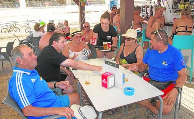 Nuria, en el centro, sirviendo unos refrescos a unos clientes, en el chiringuito La Reya, en la playa de Bahía de Puerto de Mazarrón.