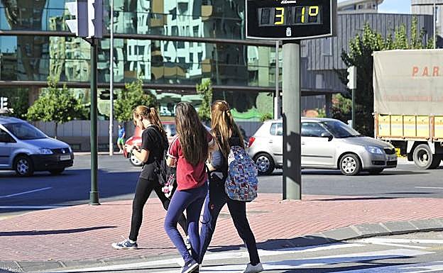 Tres jóvenes pasan junto a un termómetro, en Murcia.