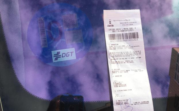 La multa, junto al distintivo azul de la DGT que identifica a los coches sin emisiones. 