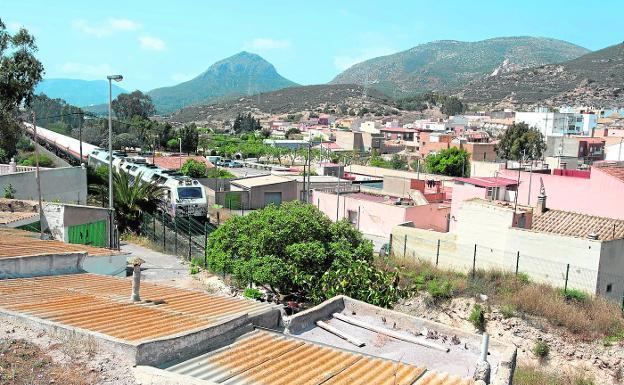 Arriba, un tren de mercancías cruza Alumbres. A la derecha, pancarta en favor del desvío del ferrocarril. 