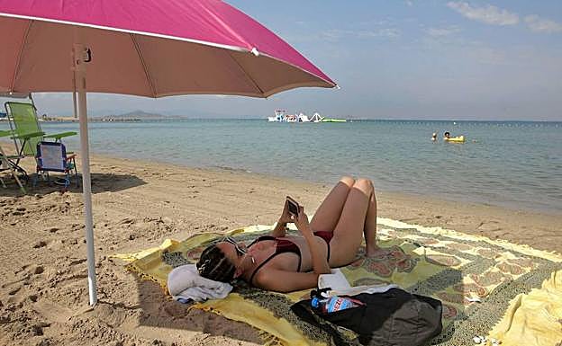 Una bañista utiliza la red wifi municipal en la playa Mistral de La Manga.