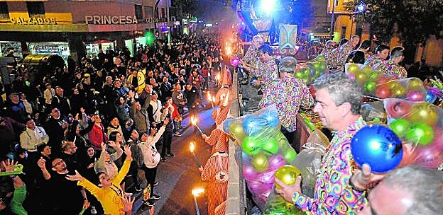 Un grupo de niños elevan las manos para recoger juguetes. 
