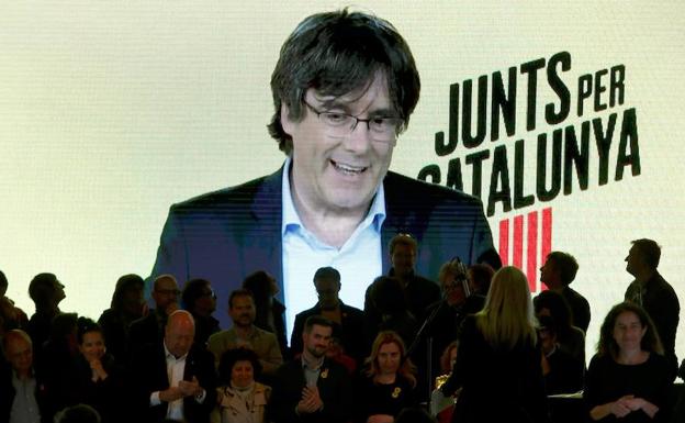 El expresidente catalán Carles Puigdemont (en la pantalla, por videoconferencia desde Bruselas) interviene en el acto de final de campaña de JxCat en Barcelona.