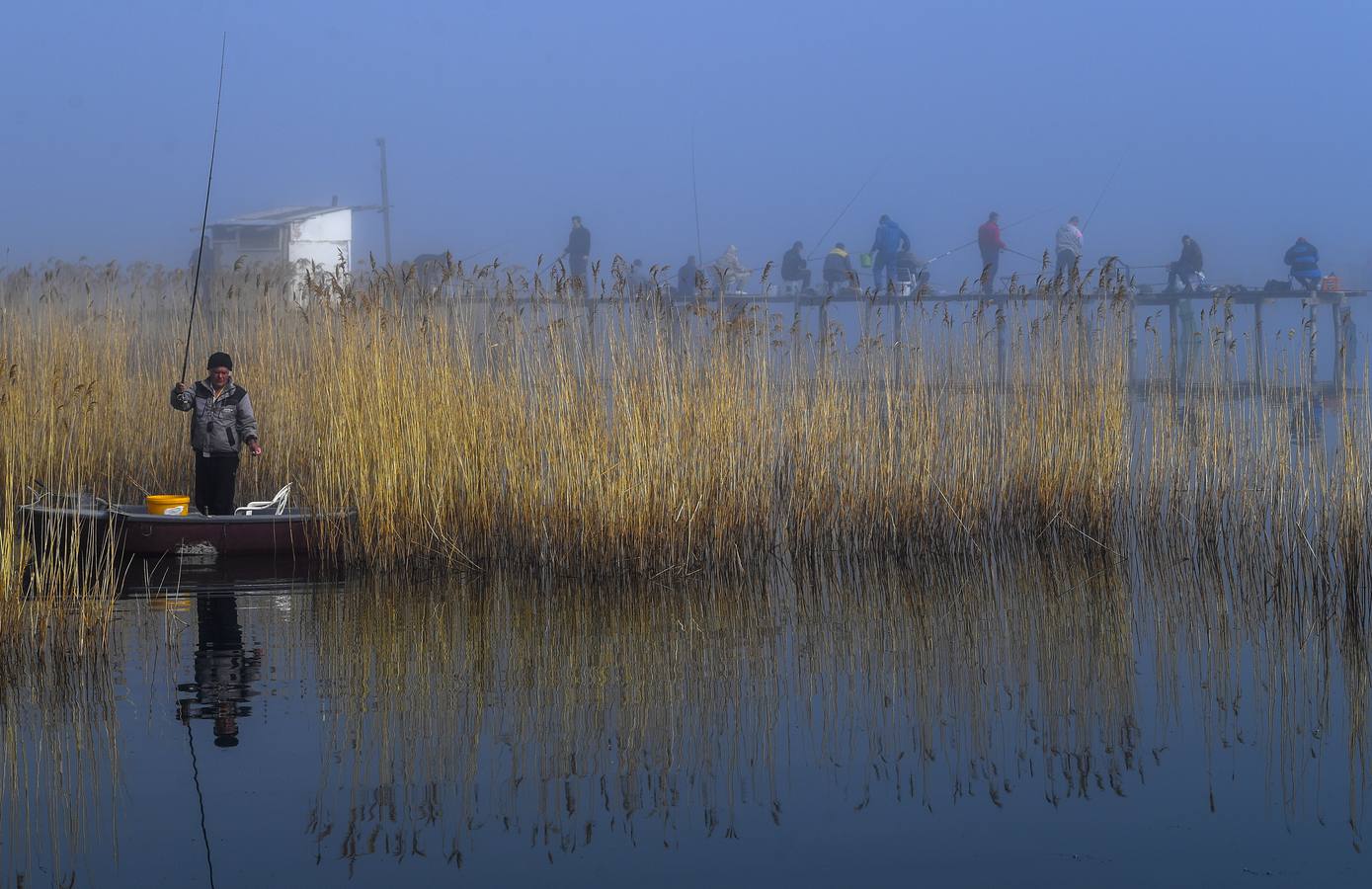 Varias personas pescan bajo la niebla en las orillas del lago Dojran, Macedonia. El lago Dojran es una reserva natural que atrae a diferentes especies de aves debido al clima relativamente cálido y la gran cantidad de peces.