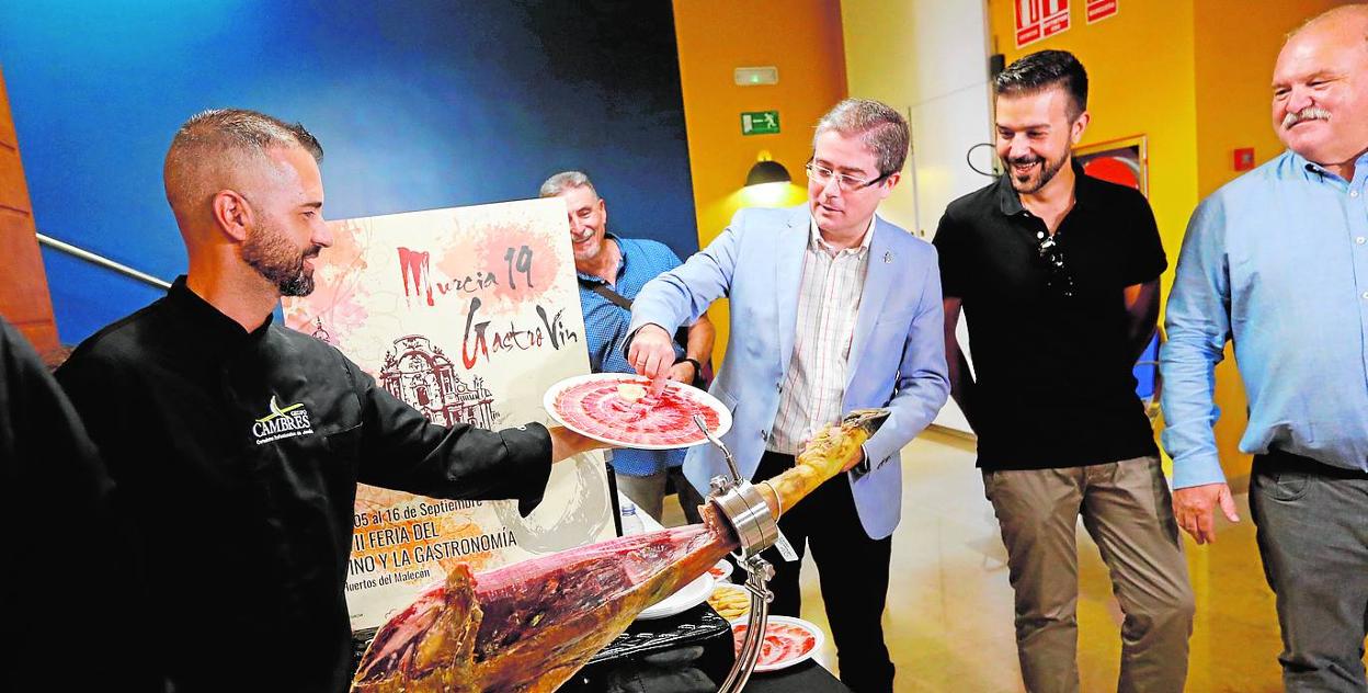 El concejal Pacheco prueba ayer jamón recién cortado. A su lado, Javier Muñoz, autor del cartel. 
