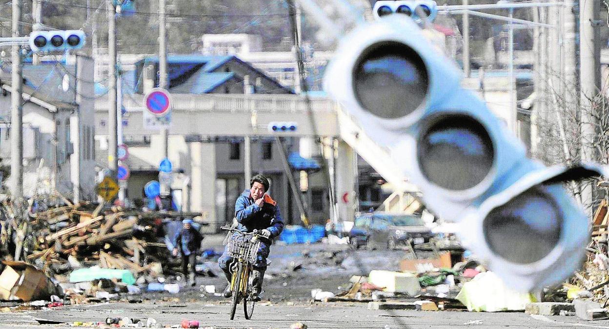 Un ciclista sortea las ruinas de Miyako tras el gran terremoto de marzo de 2011, al que siguió un devastador tsunami. Abajo, un niño se refugia bajo el pupitre durante un simulacro de seísmo en Tokio. 