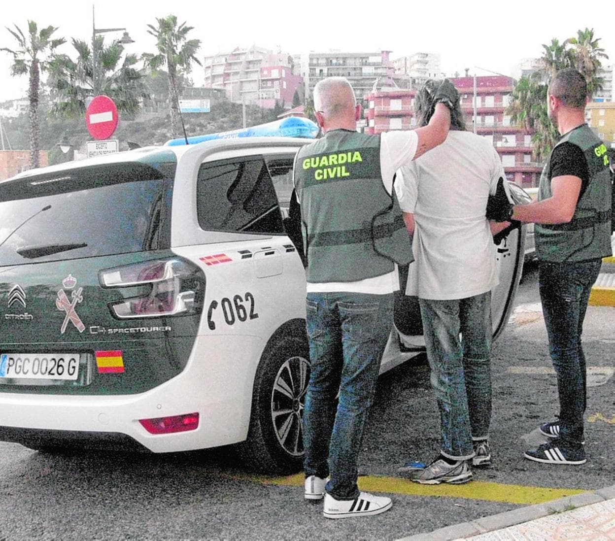 Dos guardias civiles trasladan al presunto ladrón al coche policial. 