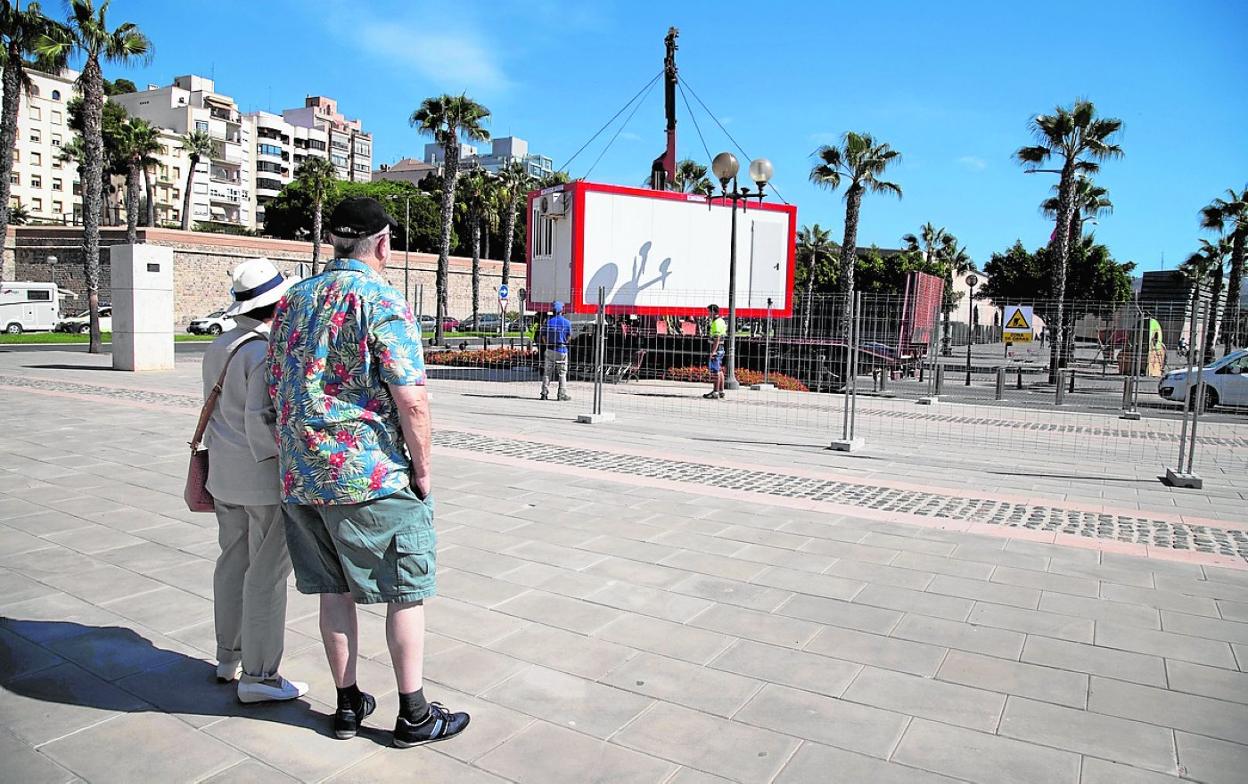 Dos turistas observan cómo descargan una caseta de obra en el Muelle de Alfonso XII. agm