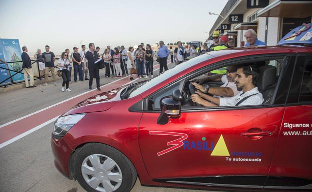 Un invidente al volante de un coche recibe las instrucciones de un profesor de autoescuela.