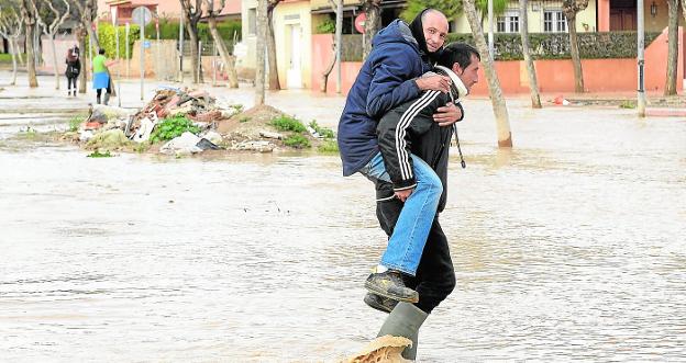 Un hombre traslada a otro 'a coscoletas' para evitar que se moje al cruzar una avenida inundada en Los Alcázares, ayer. 