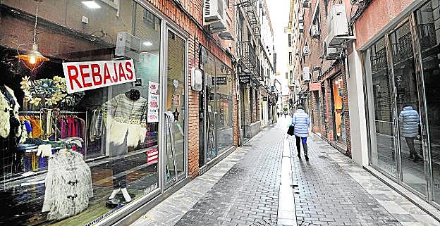 Una vecina camina por la calle Jabonerías, ayer, entre comercios vacíos con los anuncios de descuentos de rebajas en los escaparates. 