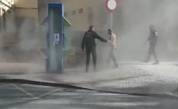 Dos agentes de la Policía Local auxilian al afectado tras prenderse fuego en la calle.
