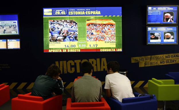 Tres jóvenes siguen un partido en una casa de apuestas.