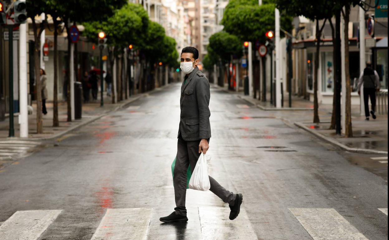 Un hombre, cargado con dos bolsas, en una calle del centro de Murcia vacía por el confinamiento por coronavirus.
