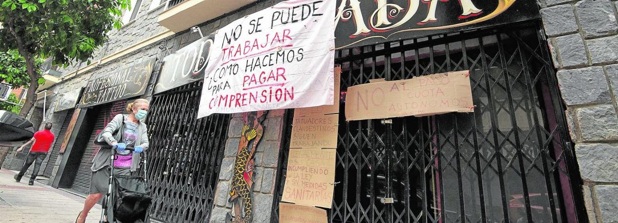 Una mujer pasa por delante de un establecimiento cerrado en Murcia, donde su dueño dejó unos carteles de protesta tras la declaración de cese de actividad. 