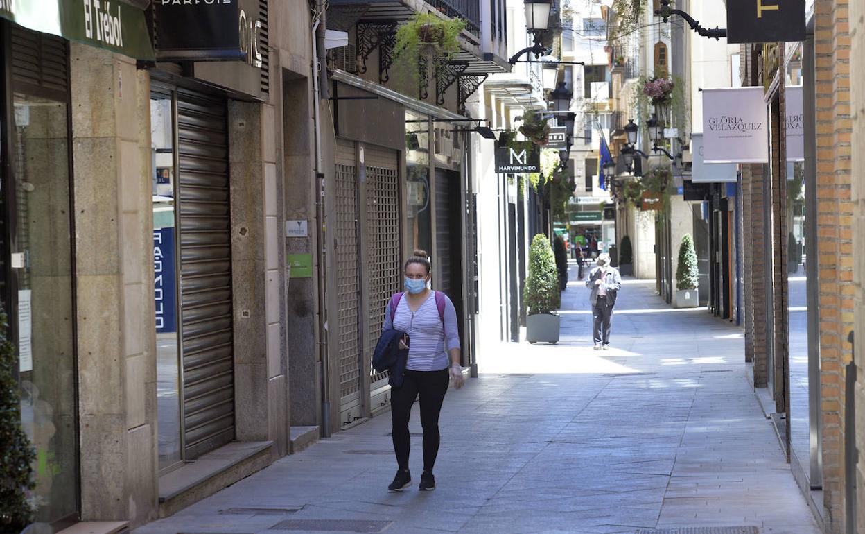 Una mujer pasea por una céntrica calle de Murcia con todas las tiendas cerradas.