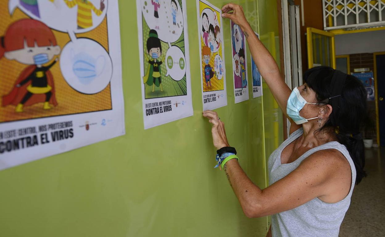 Una docente cuelga carteles informativos en el pasillo de un colegio de Murcia.