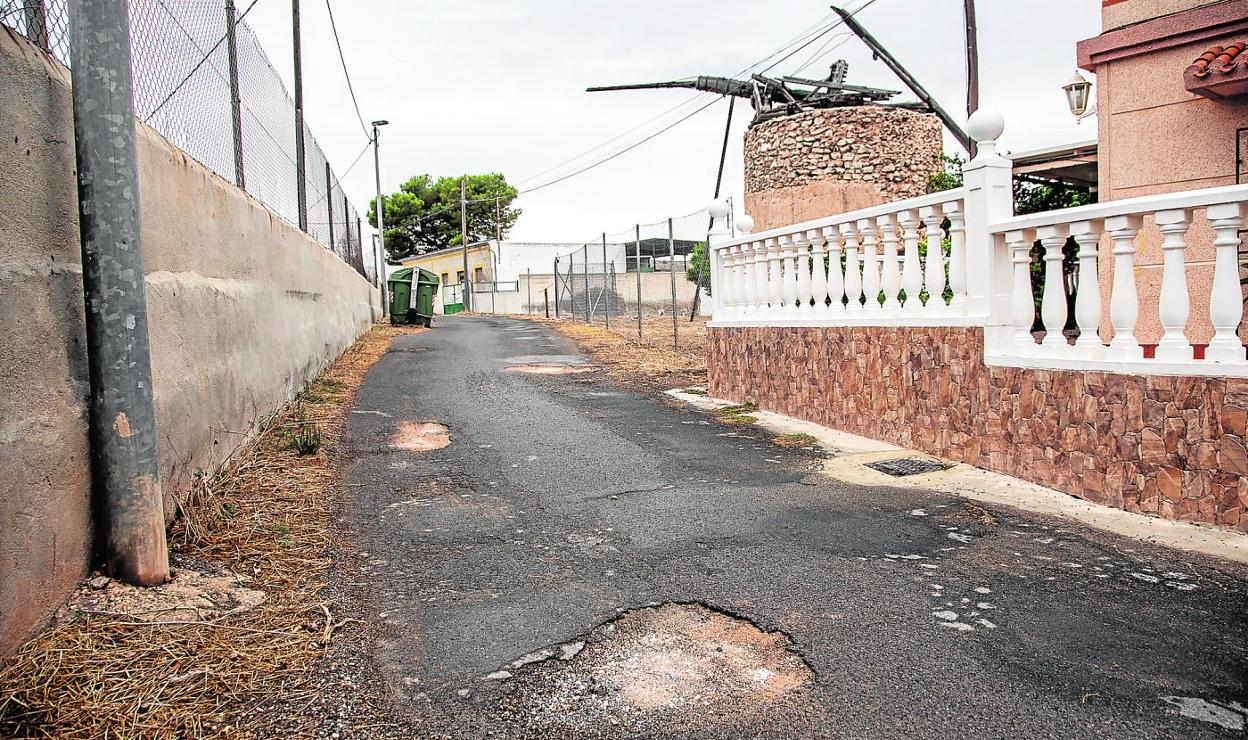 Calle del Molino, en la diputación de Galifa, llena de socavones, con el asfalto resquebrajado y con malas hierbas invadiendo la calzada. 