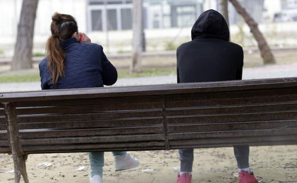 Dos jóvenes en un banco en una foto de archivo.