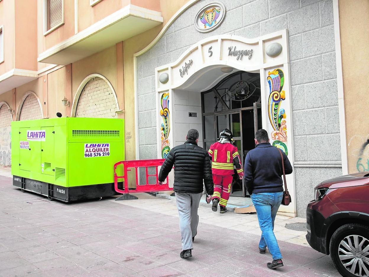 Técnicos de extinción de incendios, a su entrada al edificio, junto al generador instalado. 