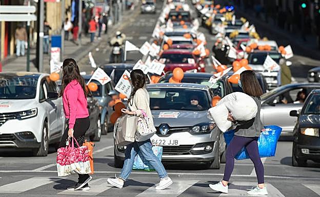 Galería. Viandantes observan la cola de coches de la manifestación mientras cruzan por un paso de peatones.