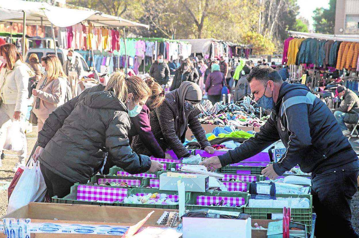 Tres clientas, frente a un vendedor, buscan en cajas en uno de los puestos del mercadillo. 