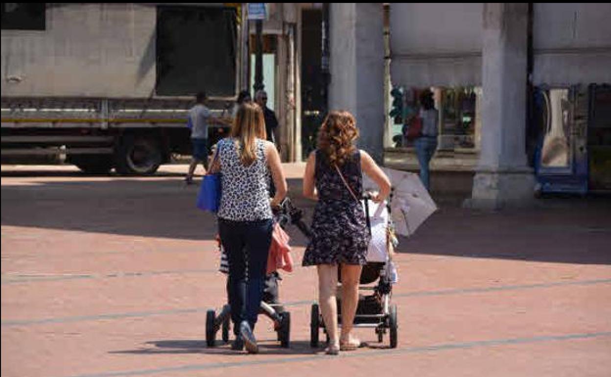 Dos madres con sus hijos paseando por una calle en una foto de archivo.