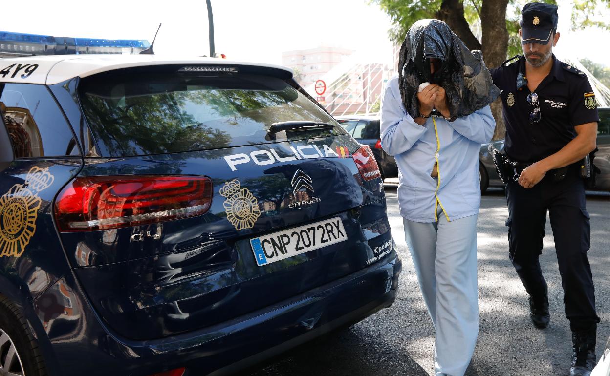 El acusado de atacar con un cuchillo a su madre es conducido por un agente para la reconstrucción de los hechos. 