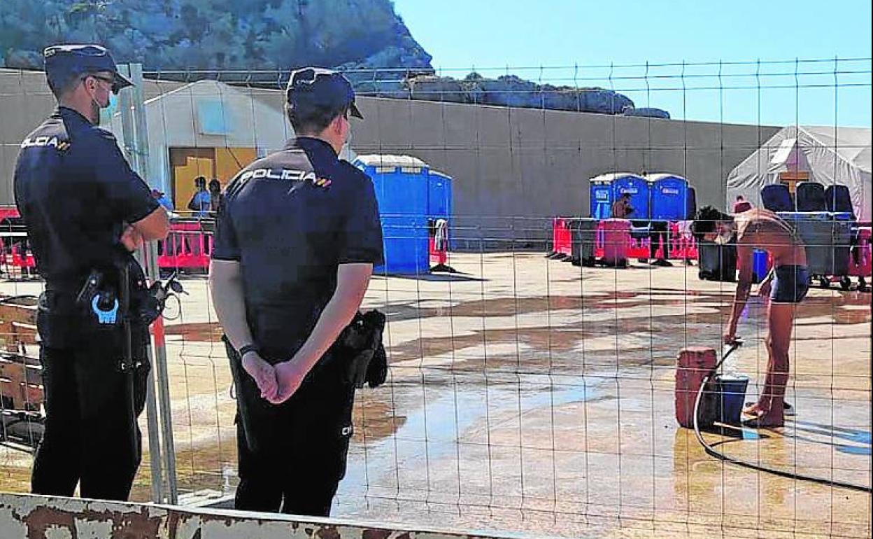 Un inmigrante se asea con una manguera en el campamento de Escombreras, custodiado por dos policías nacionales, en septiembre.