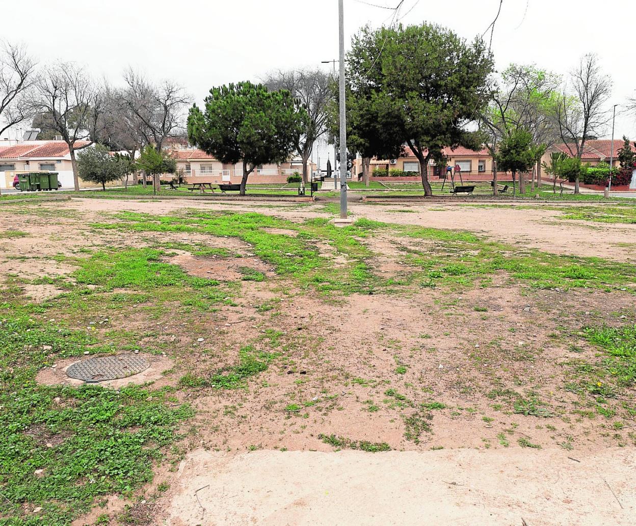 Plaza del Azadón llena de tierra y maleza y con una zona infantil al fondo envejecida y destrozada. 