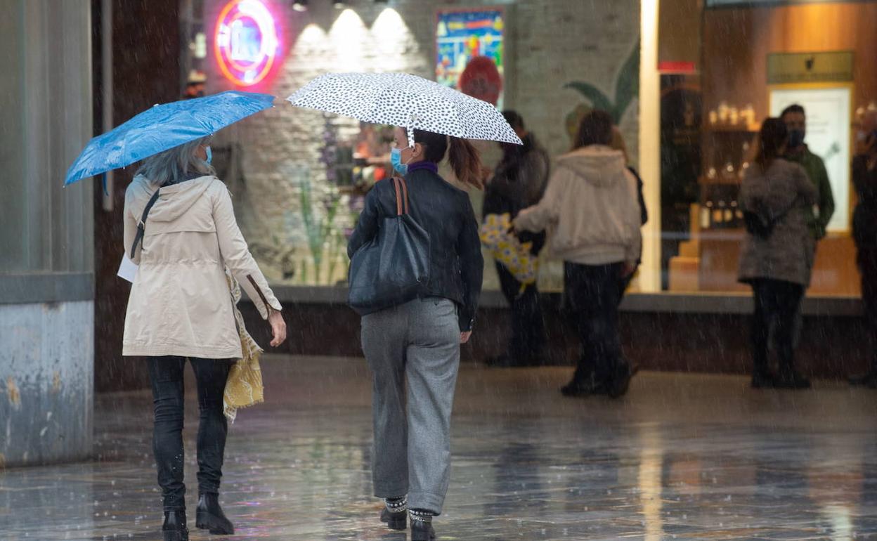 Dos personas se protegen de la lluvia con un paraguas por el centro de Murcia, en una imagen de archivo.