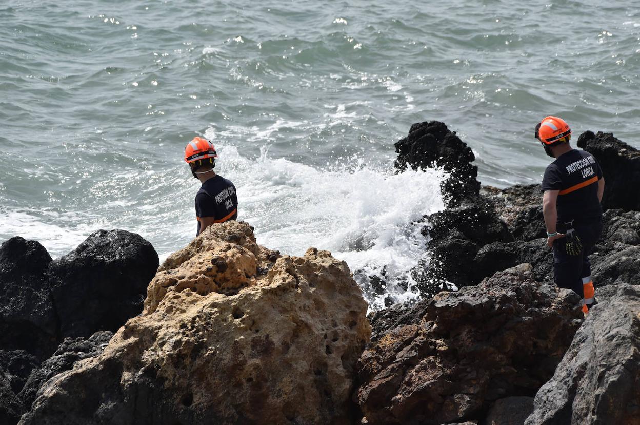 Dos voluntarios de Protección Civil buscan a los inmigrantes, ayer, entre las rocas de la costa de Mazarrón.