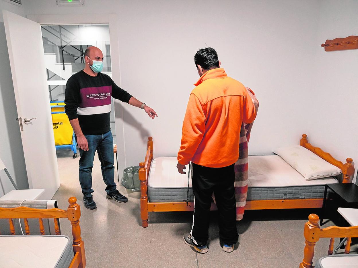 El técnico de Cáritas indica a un usuario recién llegado al albergue la cama donde va a dormir. 