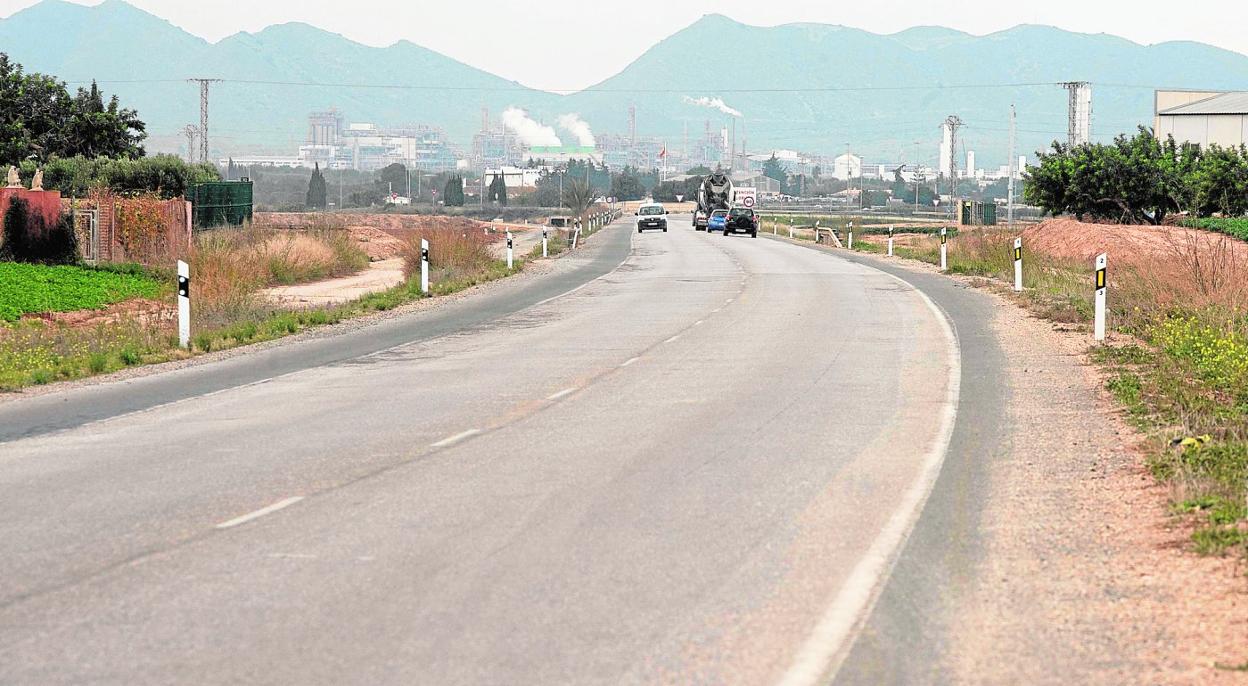 Coches y camiones atraviesan una zona con baches en la carretera de La Aljorra, con la fábrica de Sabic al fondo. 