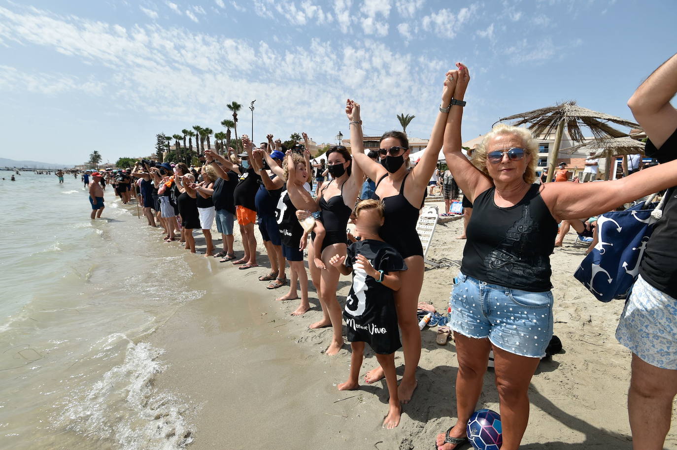 28/08/2021. Cadena ciudadana para ‘abrazar’ el Mar Menor. Vecinos y turistas unen sus manos para ‘abrazar’ de forma simbólica la laguna y exigir soluciones ante la mortandad de peces y crustáceos en el Mar Menor. «Sos Mar Menor» y «Mar Menor vivo, vertido cero» fueron algunos de los mensajes que portaron los participantes de la protesta, todos ellos ataviados con camisetas negras en señal de luto por el humedal. | JAVIER CARRIÓN