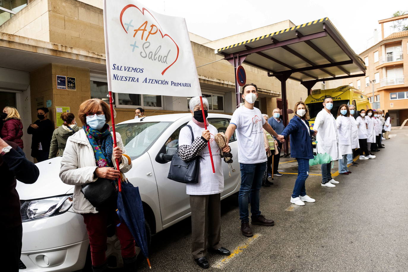 18/11/2021. Protestas por una Atención Primaria «desbordada». Decenas de pacientes y profesionales reivindicaron bajo la lluvia más recursos e inversión para una Atención Primaria «desbordada». La protesta se repitió en los centros de salud de San Diego (Lorca), Jesús Marín (Molina de Segura), Virgen de la Caridad (Cartagena) y Francisco Palao (Yecla). En un manifiesto al que se sumaron 76 organizaciones, la Marea Blanca advirtió de que este «deterioro se venía produciendo desde años antes de la pandemia, consecuencia de una financiación insuficiente, unida a la falta de adecuación y dotación de recursos humanos y materiales». Ahora, «la pandemia ha evidenciado las debilidades crónicas de la Atención Primaria y ha anulado las mejoras que se estaban implantando en los últimos años». | ROS CAVAL