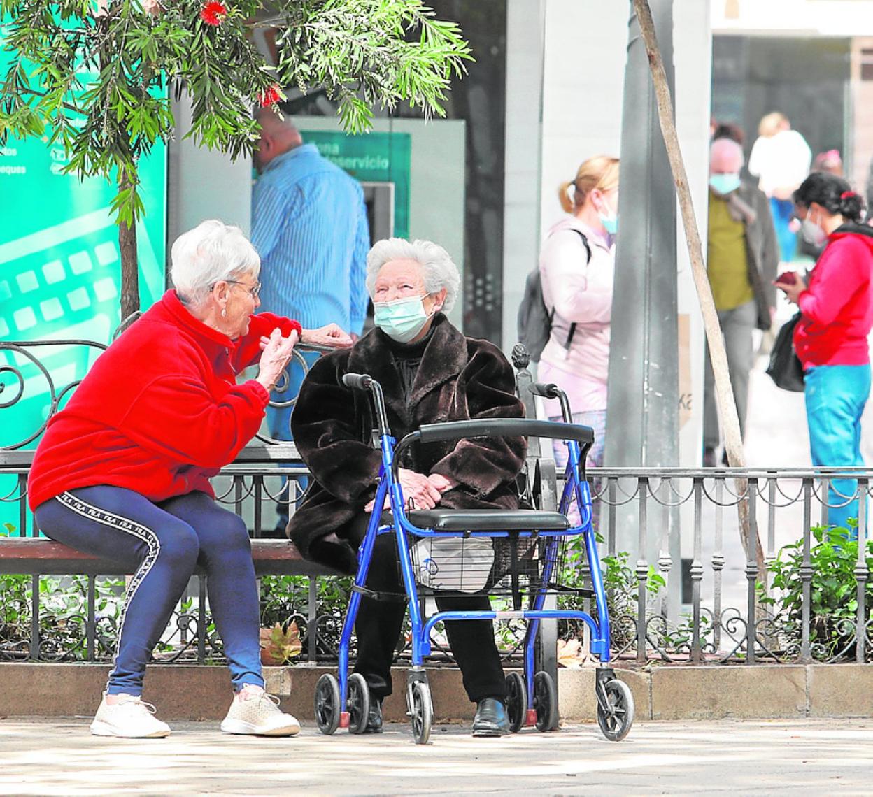 Dos personas mayores descansan en el banco de una plaza. 