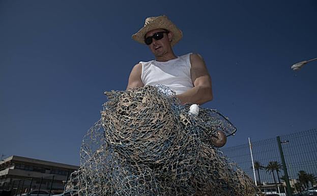 Carlos López muestra una de sus redes, infestada de algas. 