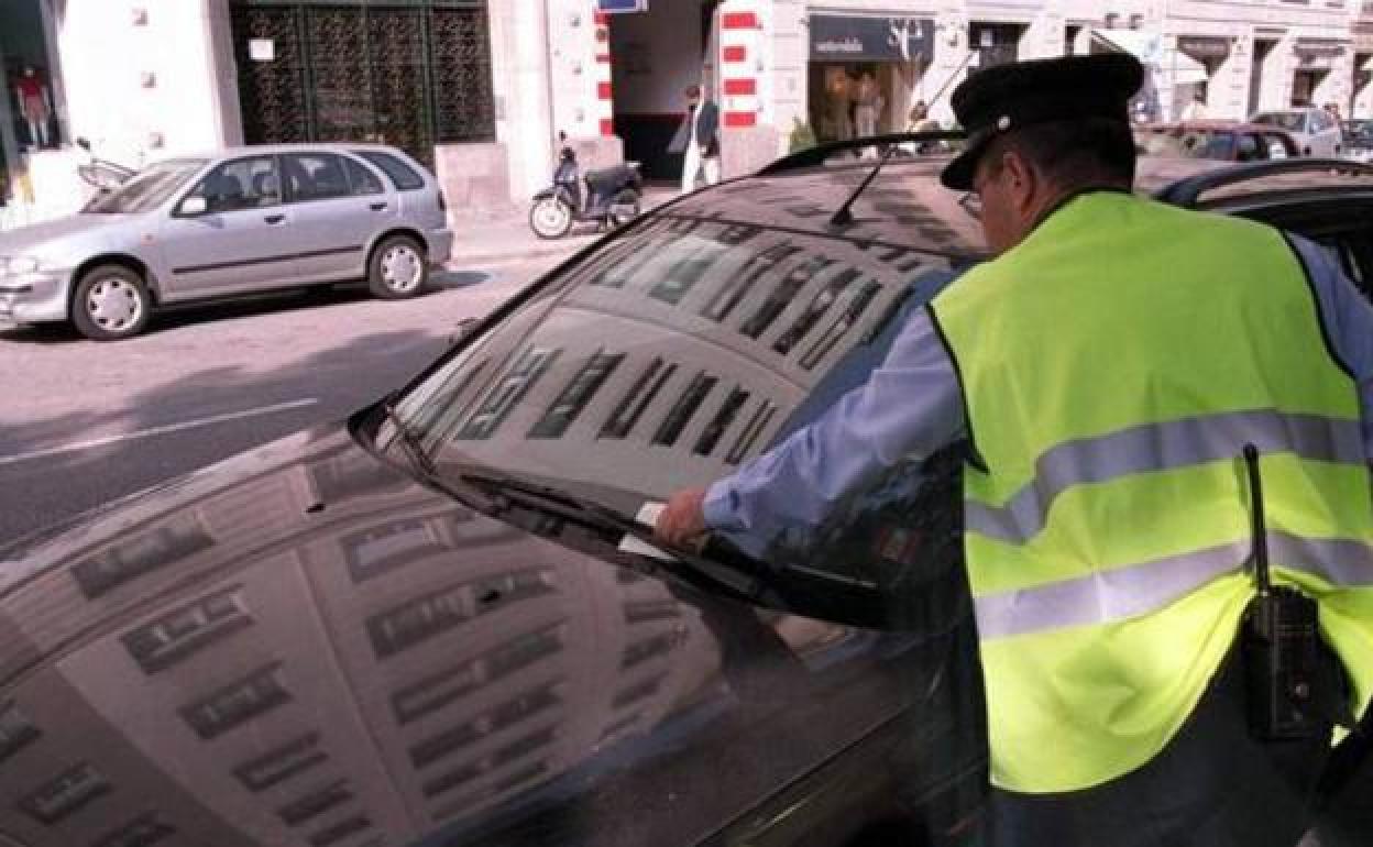 Un agente pone una multa a un vehículo estacionado. 