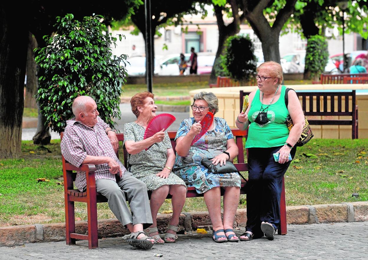 Un grupo de mayores combate el calor con abanicos en un jardín de San Basilio mientras conversan. 