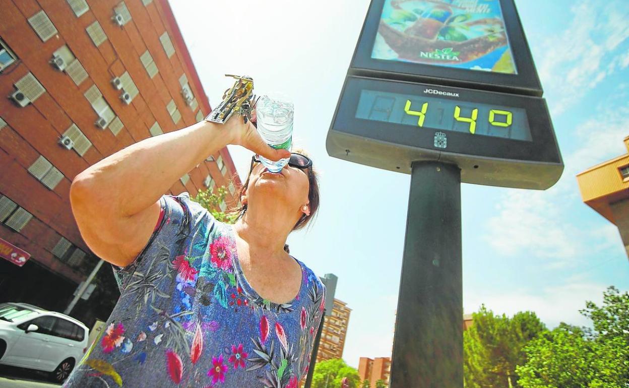 Una mujer bebe agua ante un termómetro que marca 44 grados en Murcia. 