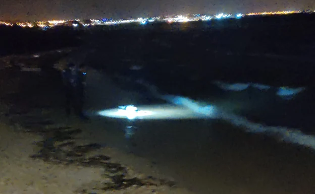 Dos agentes observan el cuerpo hallado en la playa de El Mojón.