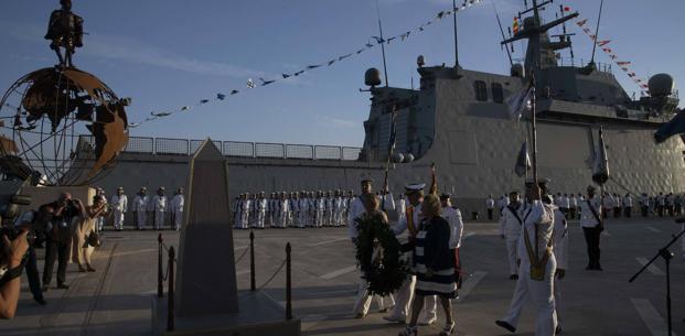 La alcaldesa, Noelia Arroyo, el almirante Juan Luis Sobrino, y la presidenta del Puerto, Yolanda Muñoz, depositan una corona de laurel a los pies de un monolito, en homenaje a los que dieron su vida por España, en el acto de rendición de honores al marino español que culminó la primera vuelta al mundo. Detrás, la fuerza militar y el buque 'Furor'.