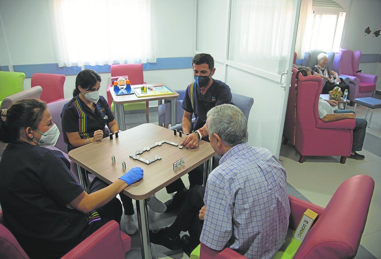 Tres empleados juegan al dominó con uno de los residentes, en una sala de estar. 