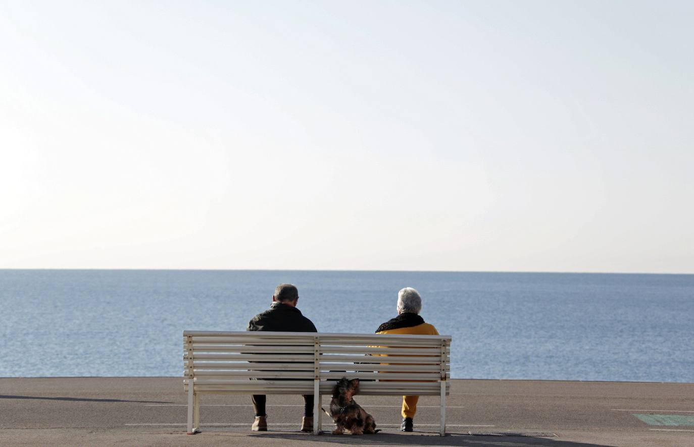 Una pareja sentada frente al mar junto a su perro, en una foto de archivo..