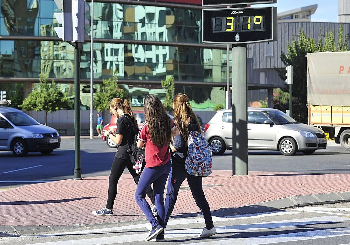 Tres jóvenes pasan junto a un termómetro que marca 31 grados en Murcia, en una imagen de archivo.